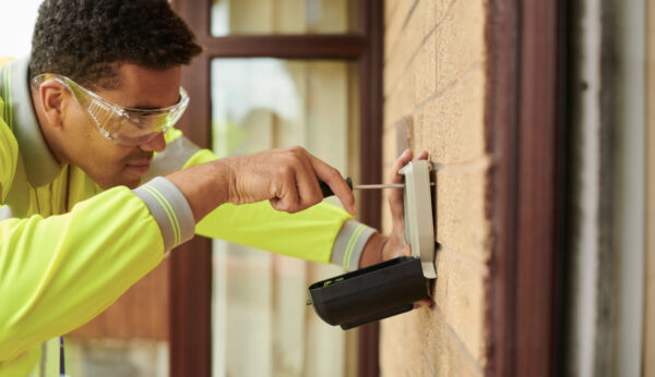 Man installing sprinkler system controller on exterior wall