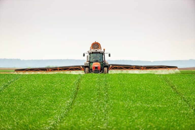 Large tractor with wide boom arms applying fertilizer to a lush green field, emphasizing the careful calibration and equipment maintenance required for precision fertilization.
